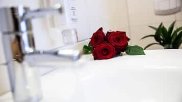 Une salle de bain avec un lavabo blanc, un robinet moderne et un bouquet de roses rouges.