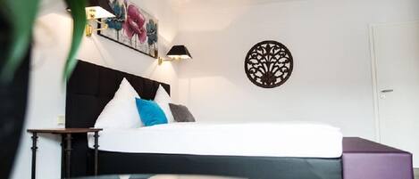 Een moderne slaapkamer met een groot bed, een nachtkastje en een decoratief wandobject.