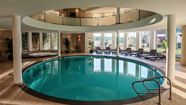 Una amplia piscina interior con solárium, tumbonas y plantas en macetas.