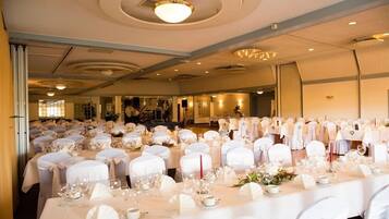 Uma sala de banquetes com mesas redondas preparadas para um evento formal, com toalhas brancas e capas de cadeiras combinando.