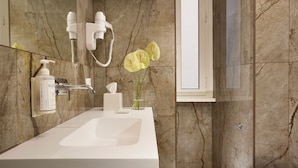A modern bathroom with a marble sink, a hairdryer, and a vase with flowers. - Velantia Vaticano - Guesthouse (Rome)