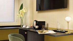 A modern hotel room with a dark wooden desk, a flat-screen TV, a vase with flowers, a coffee maker, and a magazine. - Velantia Vaticano - Guesthouse (Rome)