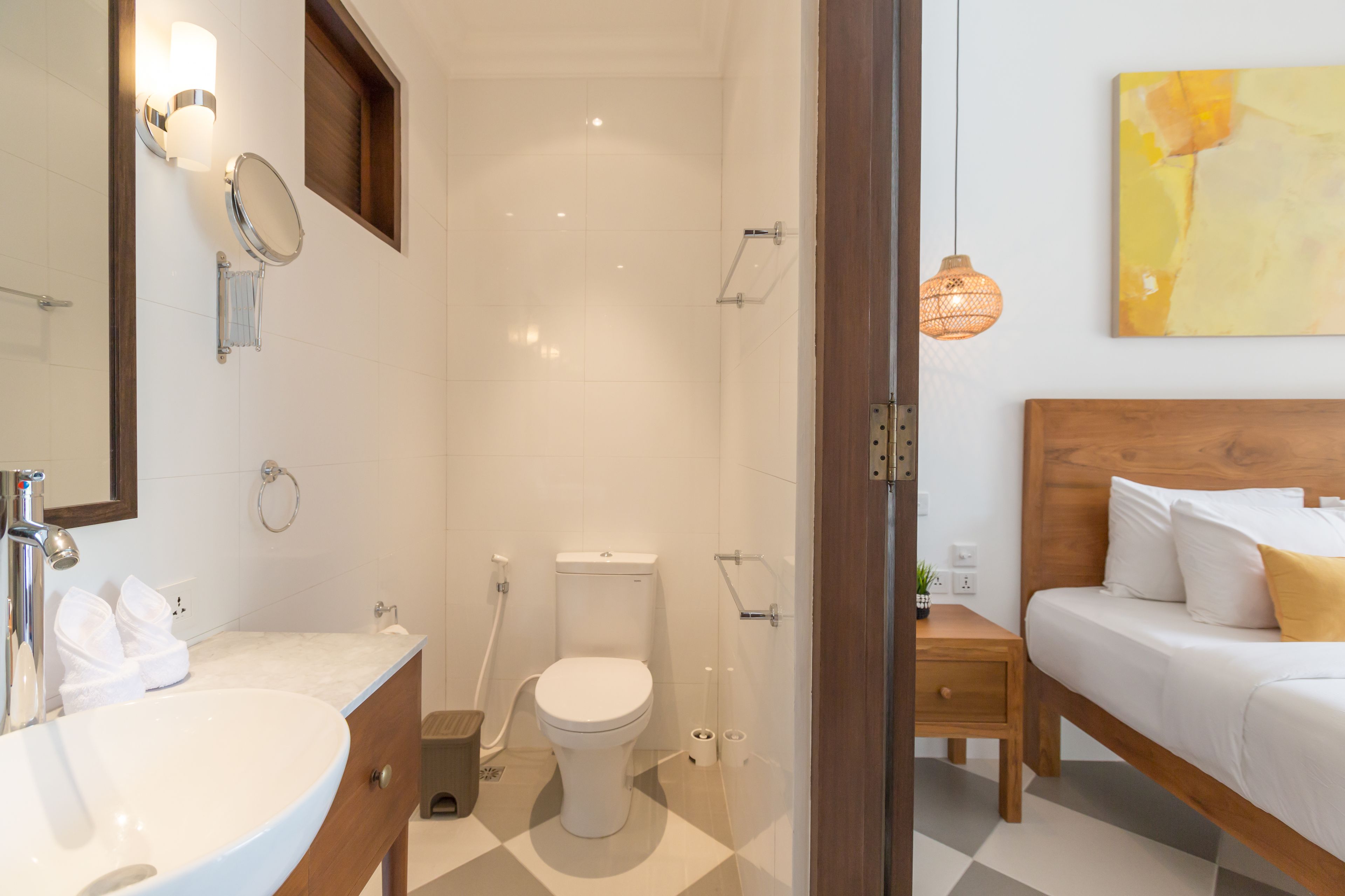 Ein Badezimmer mit Waschbecken, Toilette und Dusche. Ein Holzbett mit weißen und gelben Kissen.
