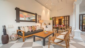 A spacious living area with a sofa, coffee table, and dining set. There is a kitchen area in the background with a dining table and chairs. - Villa CJ (Seminyak)