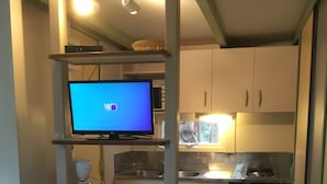 Una cocina compacta con televisión integrada, cafetera y refrigerador pequeño.