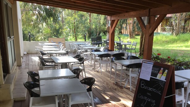 Un patio exterior con mesas y sillas, una pérgola de madera y un cartel.