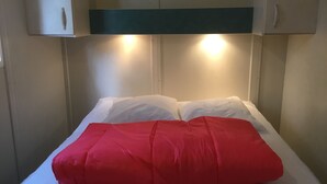 Una cama con ropa blanca de cama y una manta roja, cabecera blanca y dos lámparas de pared.