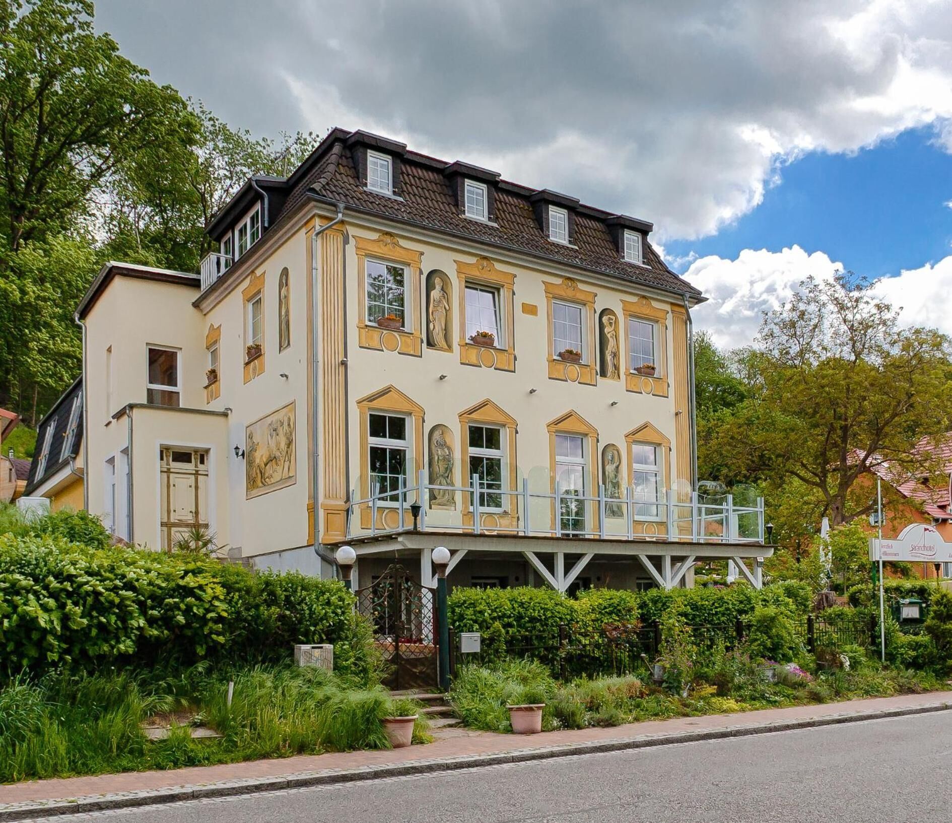 A two-story building with a balcony, surrounded by greenery.