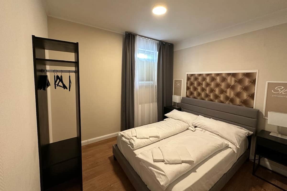 A modern hotel room with a large bed, a wardrobe, and a headboard with a tufted design.