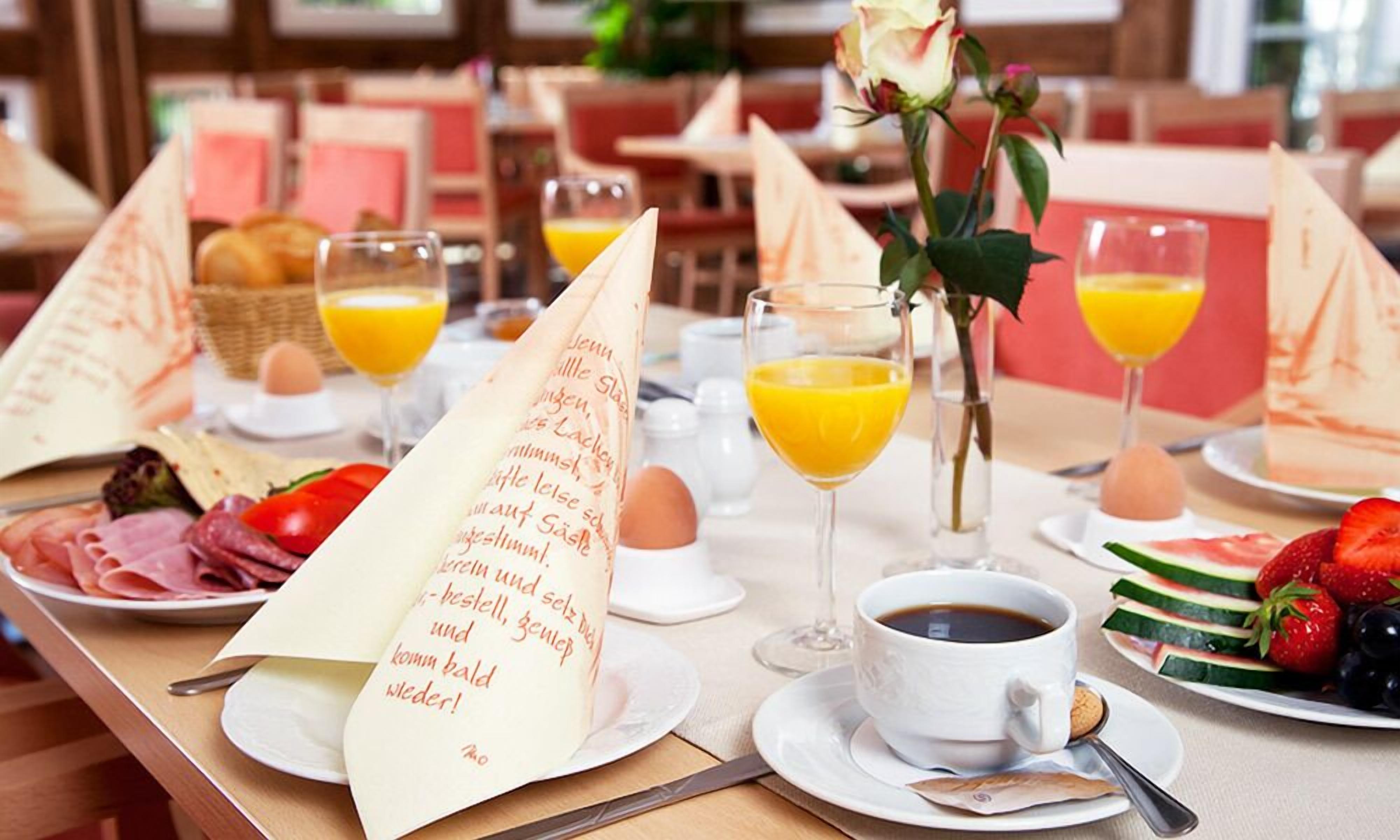 A breakfast setting with a menu, plates of food, glasses of orange juice, and a vase with a rose.