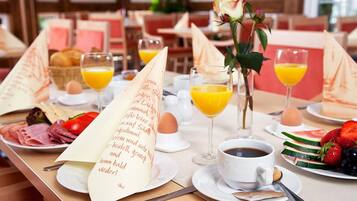 A breakfast setting with a menu, plates of food, glasses of orange juice, and a vase with a rose.