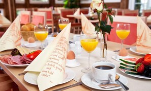 A breakfast setting with a menu, plates of food, glasses of orange juice, and a vase with a rose. - Strandhotel Buckow Resort & SPA (Buckow)