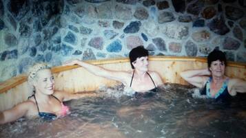 Three people in a stone-walled hot tub with wooden benches.