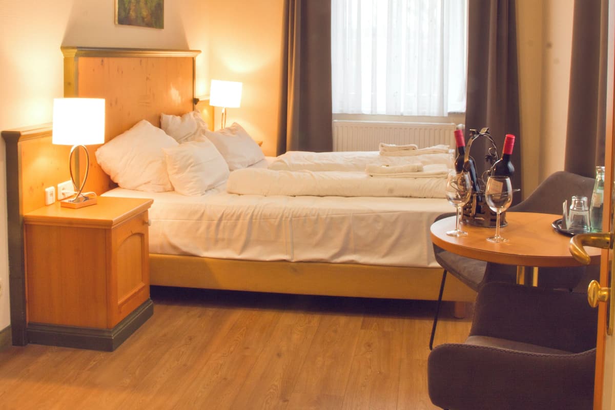 A hotel room with a wooden floor, two beds, a desk with a chair, a TV, and a window with curtains.