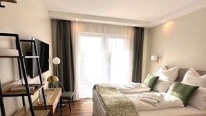Une chambre d’hôtel avec un lit, un bureau et une chaise, une télévision et une fenêtre avec des rideaux.