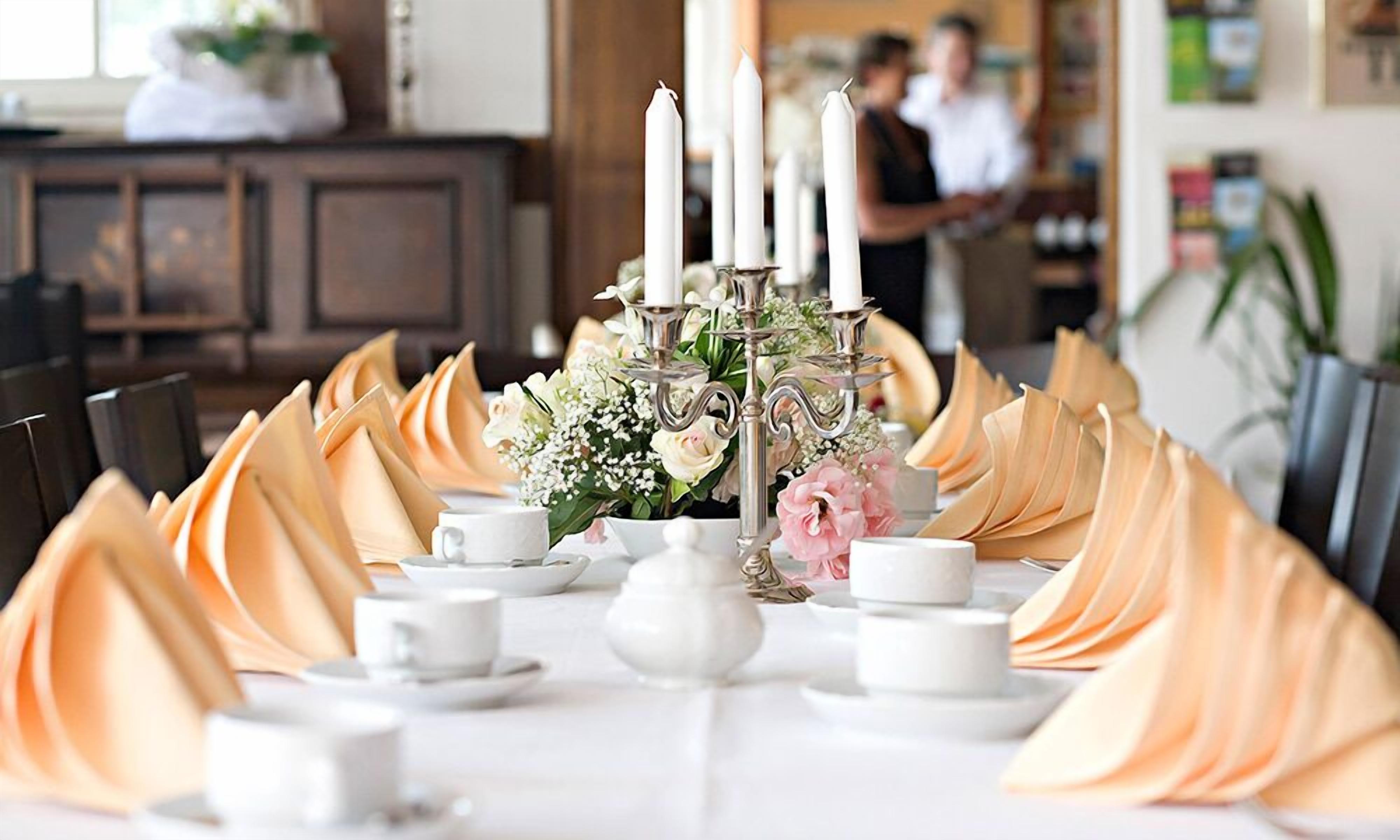 A dining table set with white plates, cups, and a centerpiece with flowers and candles.