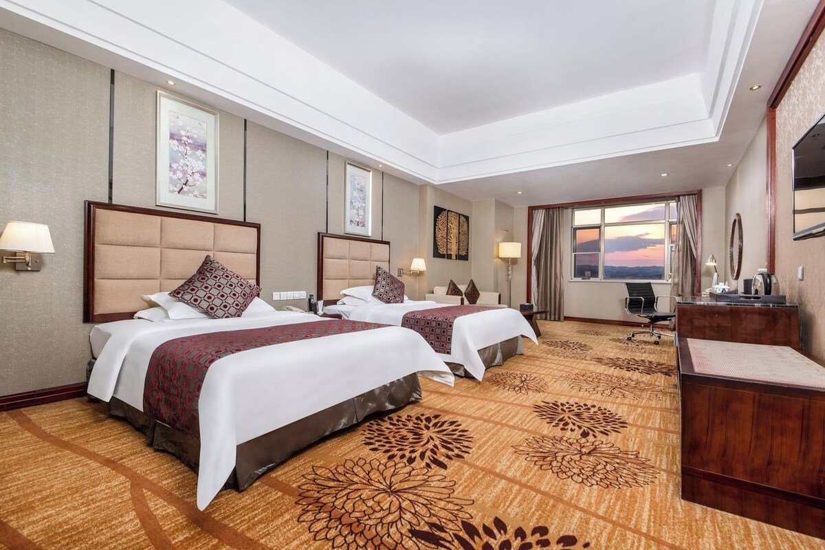 Una habitación de hotel con dos camas, un escritorio y vistas al atardecer.