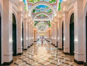 Een statig portaal met marmeren vloeren en versierde plafonddecoraties, met een centrale fontein en symmetrische architectuur.