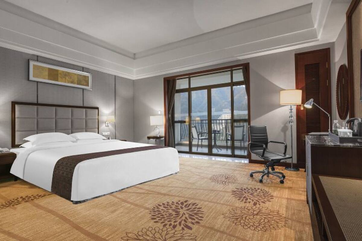 Habitación de hotel con una cama grande, un escritorio, una silla, un sofá, un balcón con vistas y un televisor.