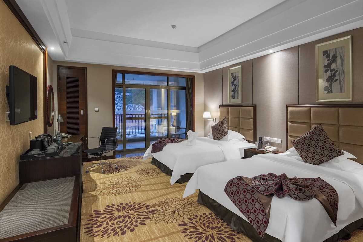 Habitación de hotel con dos camas, un escritorio, una silla, un televisor y un ventanal con vistas.