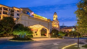 A grand hotel entrance with a prominent archway, a clock tower, and illuminated signage.