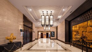 A spacious lobby with a marble floor, a large chandelier, and a decorative golden sculpture.