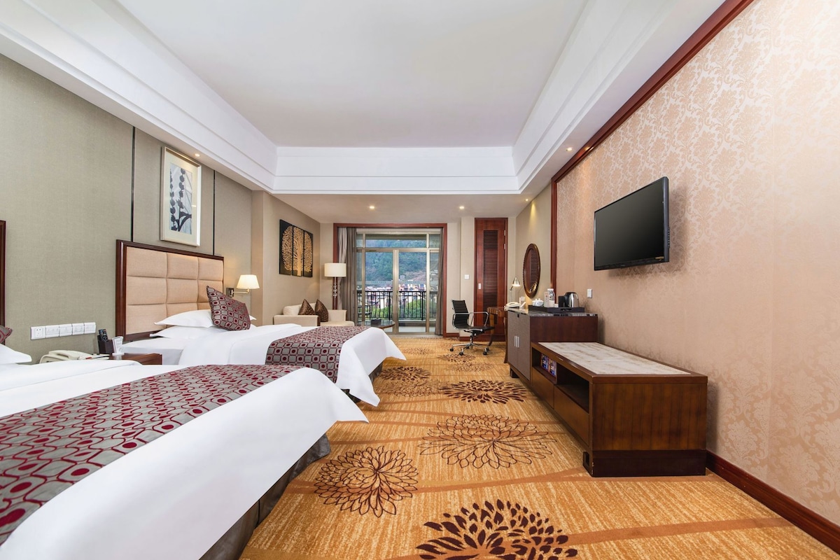 Habitación de hotel con dos camas, un escritorio, una silla, un televisor y vistas al exterior.