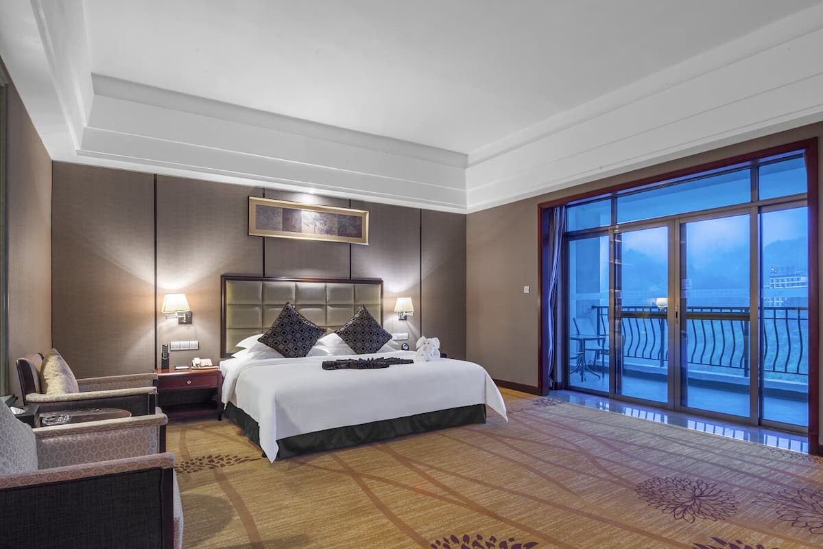 Habitación de hotel con una cama grande, dos mesitas de noche, una silla, un ventanal con vistas y una lámpara en el techo.