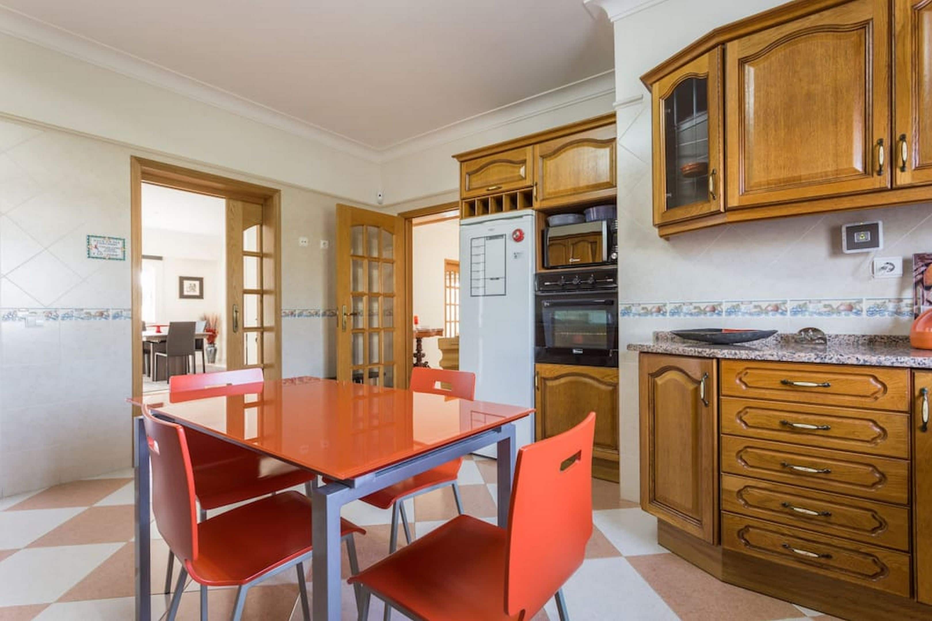 Une cuisine avec des meubles de rangement en bois, un réfrigérateur, un four à micro-ondes et une table à manger entourée de chaises rouges.