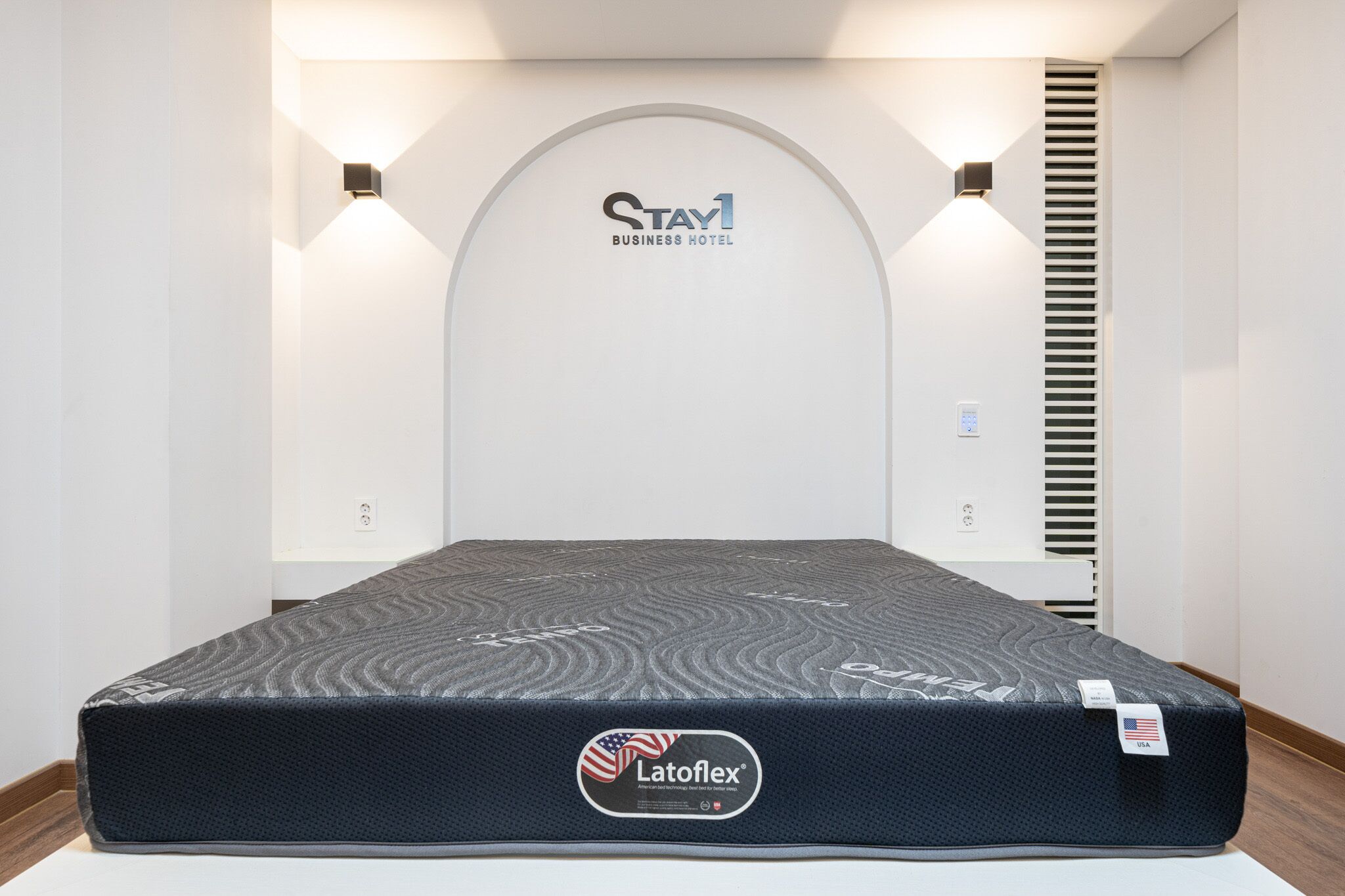 Eine LatoFlex-Matratze in einem Hotelzimmer mit einem Stay1 Business Hotel-Schild über dem Bett.
