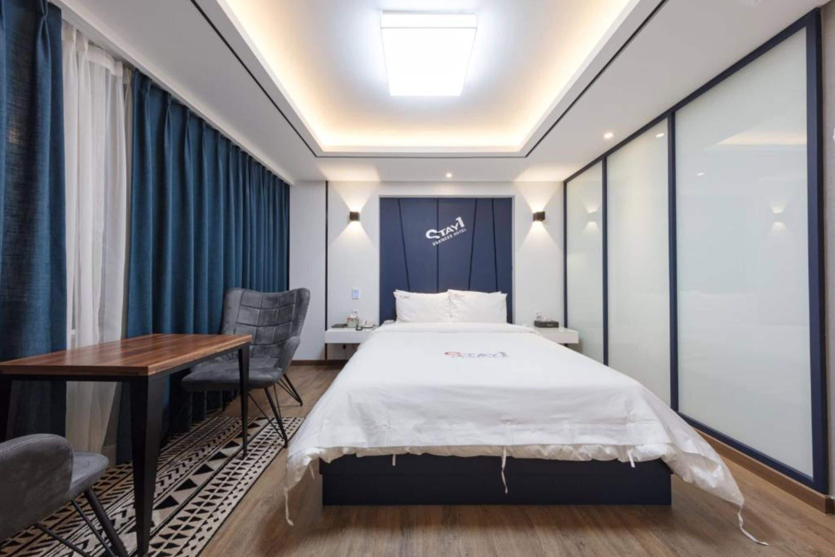 A hotel room with a bed, a desk, a chair, and a nightstand.