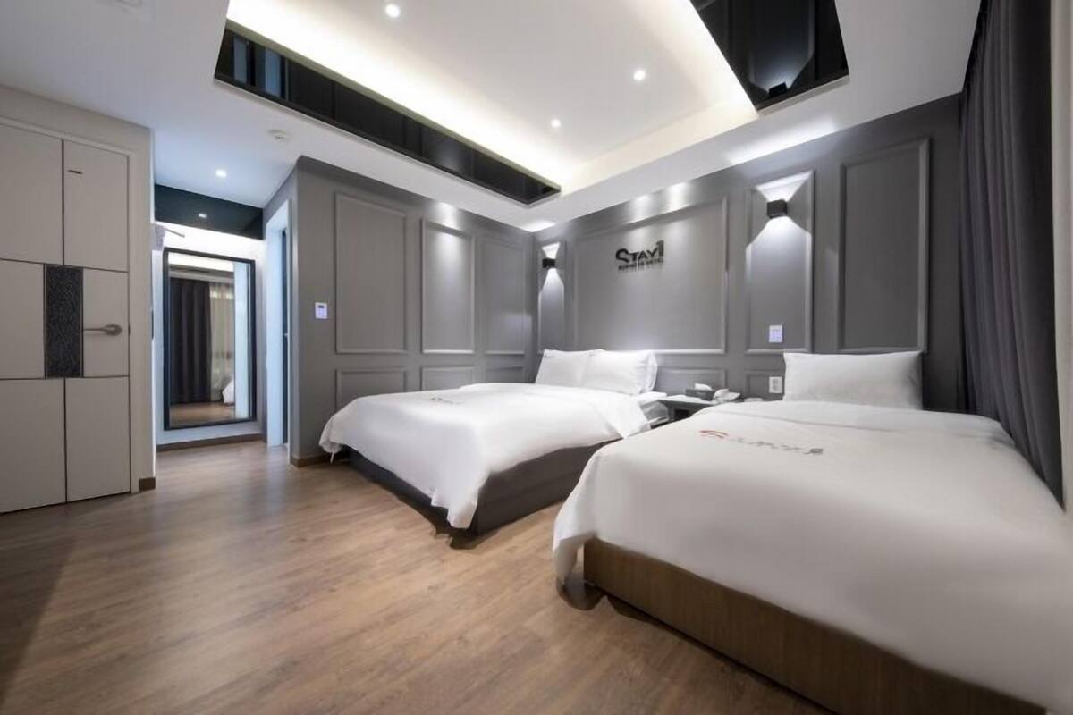 A modern hotel room with two beds, a wardrobe, and a large mirror.