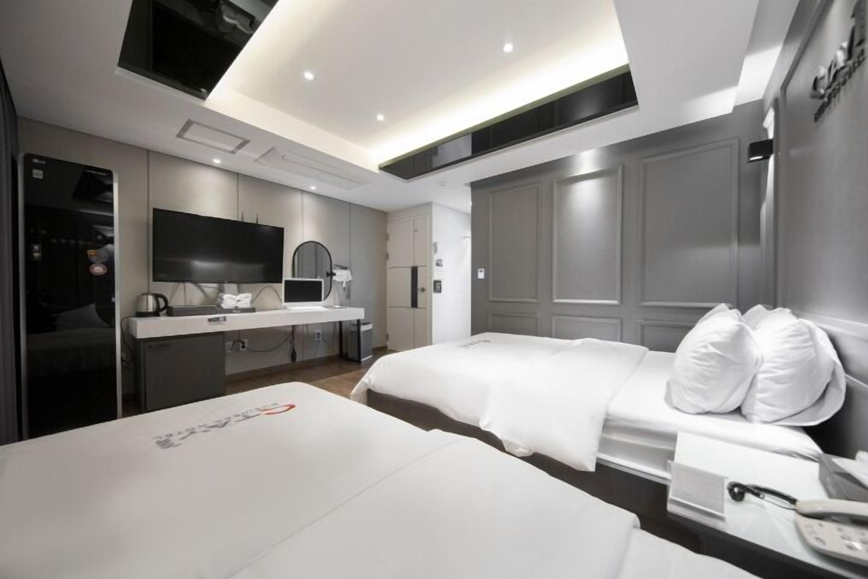 A modern hotel room with a large bed, a desk with a flat-screen TV, a kitchenette, and a bathroom.