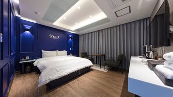 A modern hotel room with a large bed, a desk, a chair, and a TV.