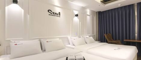 A hotel room with a large bed, two smaller beds, a chair, and a desk.