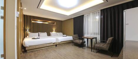 Habitación de hotel con dos camas, una mesita, una silla y un ventanal con cortinas.