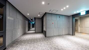 A modern hotel corridor with a patterned carpet, grey walls, and recessed lighting.