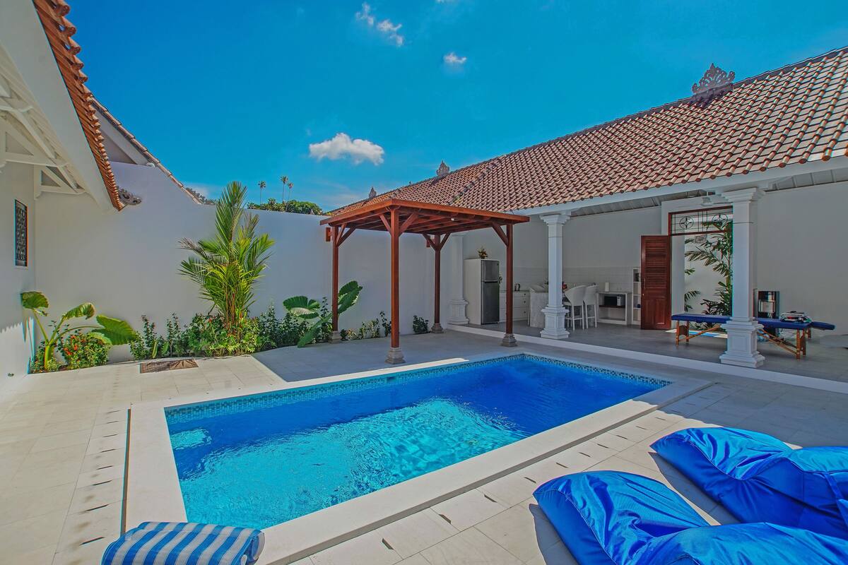 Una piscina con pérgola, mobiliario exterior y techo de baldosas.