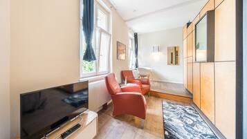 Ein modernes Wohnzimmer mit einem Flachbildfernseher, roten Sesseln, einem kleinen Tisch und einem Fenster mit Vorhängen.