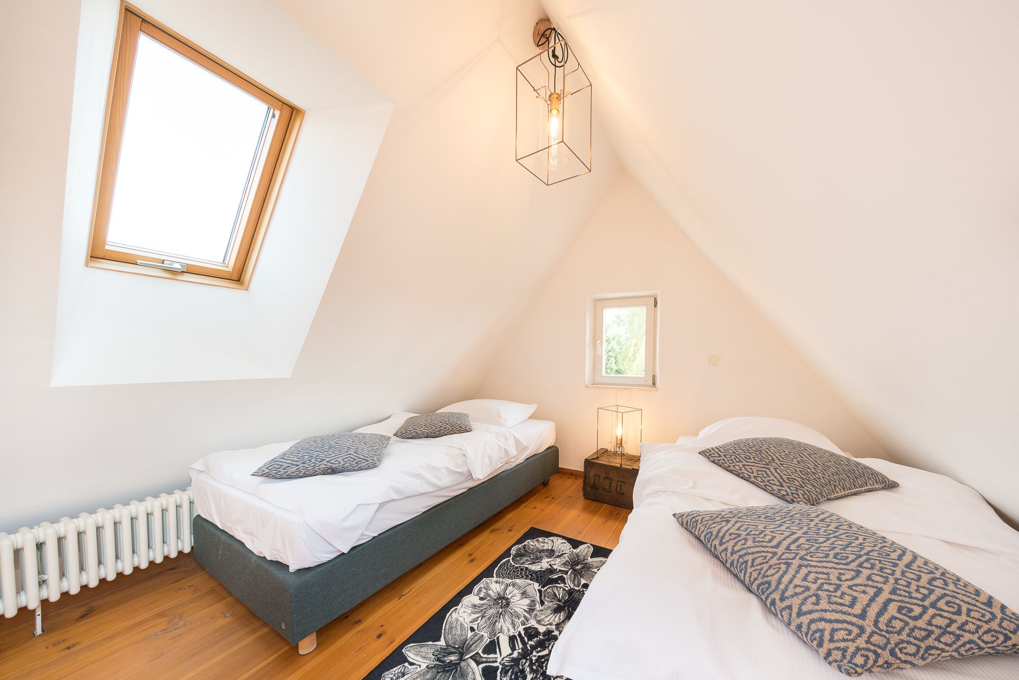 A bedroom with two beds, a radiator, a window, and a wall-mounted light fixture.