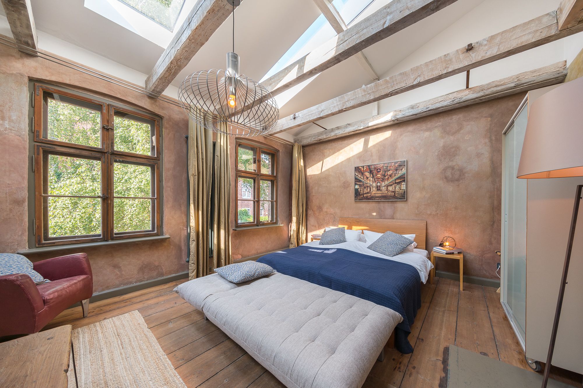 Une chambre avec un grand lit, une lucarne et un tableau accroché au mur.