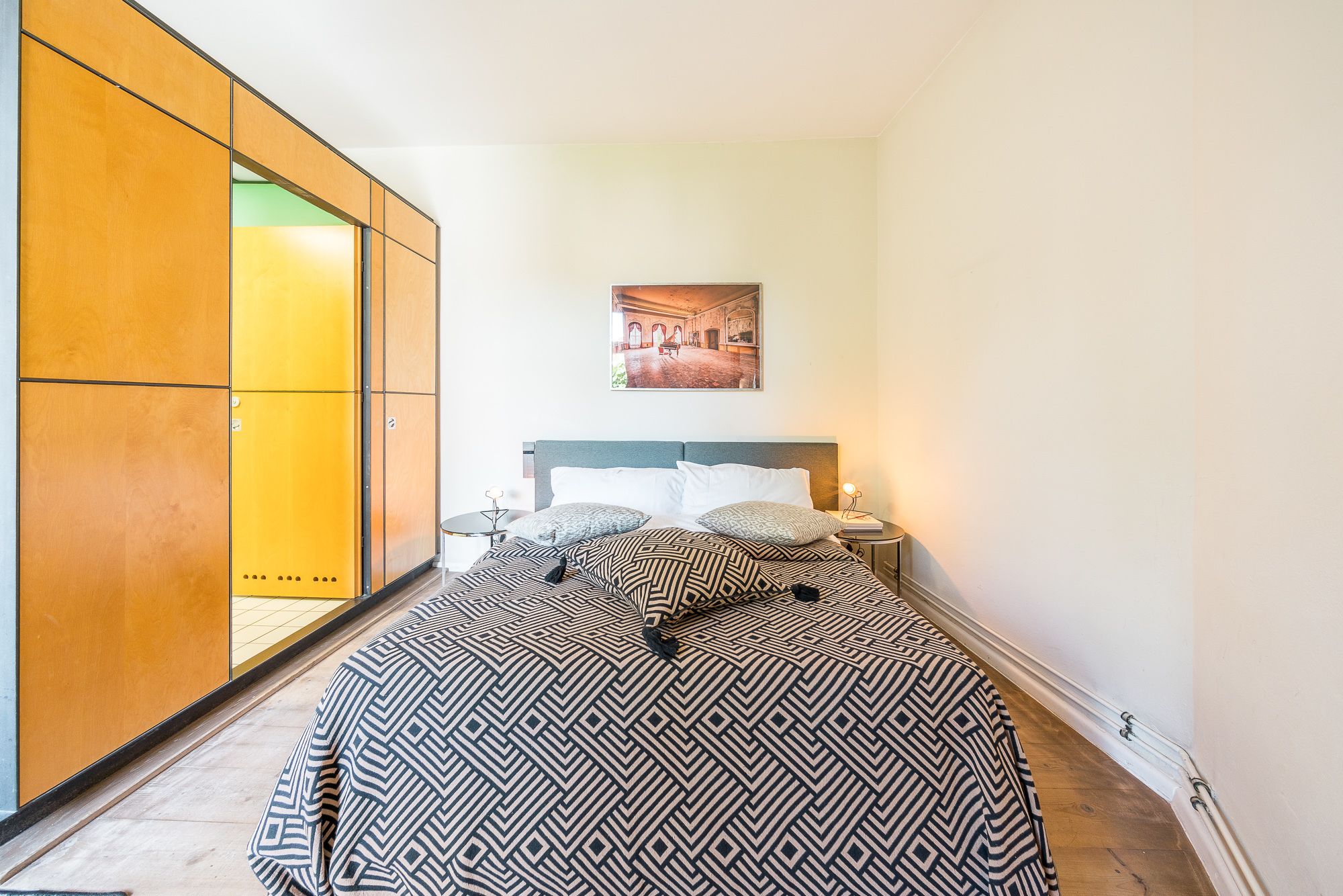 A bedroom with a bed, a nightstand, a picture on the wall, and a wardrobe.