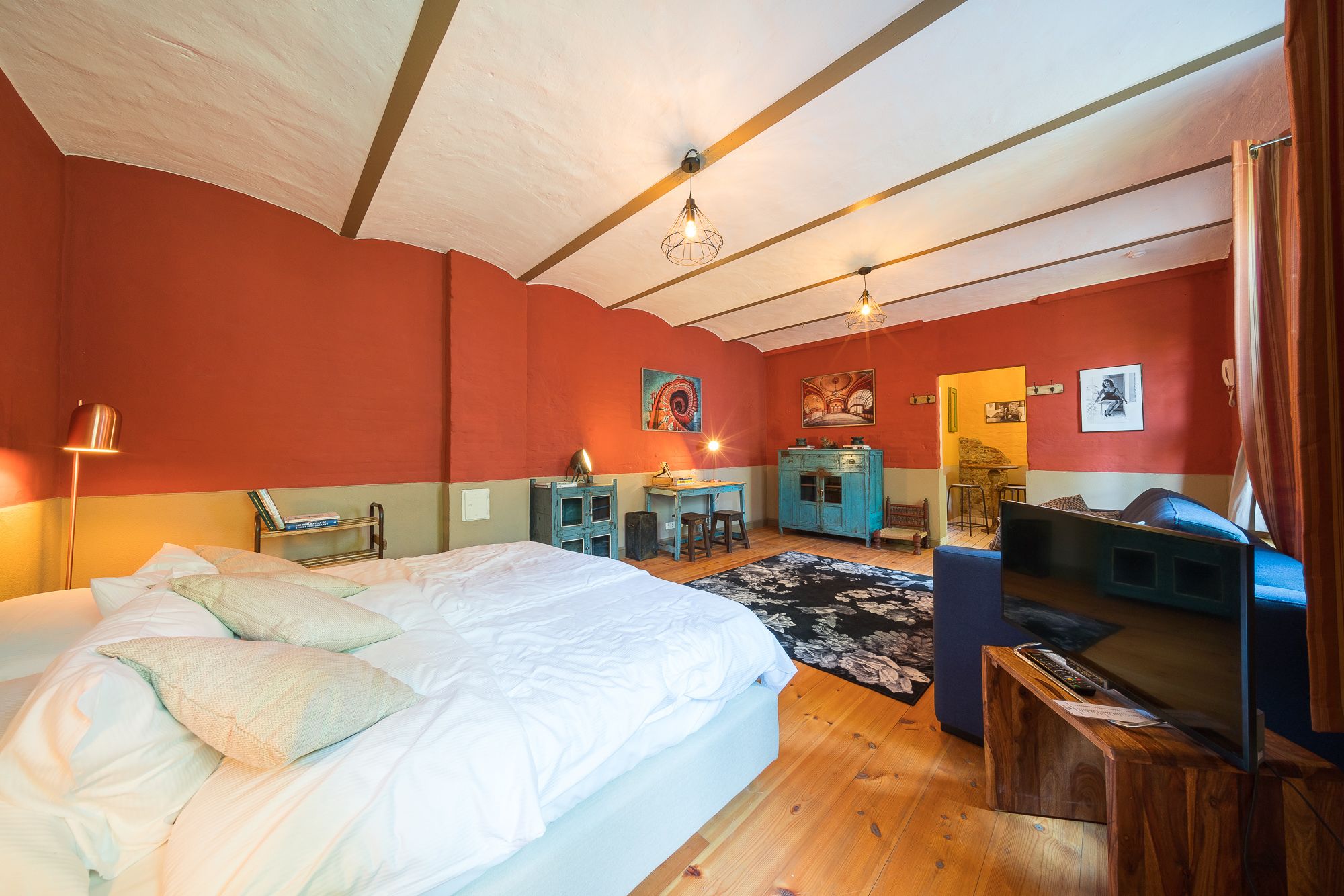 A bedroom with a large bed, a desk, a TV, and a wardrobe.
