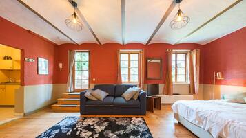 Una habitación con sofá, cama, piso de madera y ventana con cortinas.