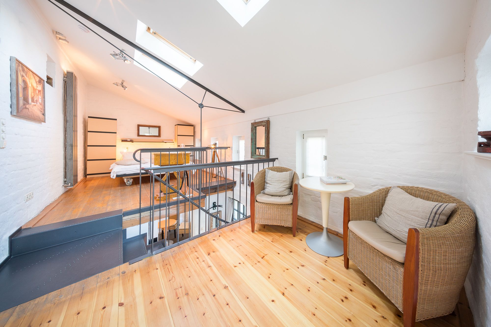 Ein geräumiger Loft mit Holzboden, einer Treppe, einem Bett, einem Korbstuhl und einem kleinen Tisch.