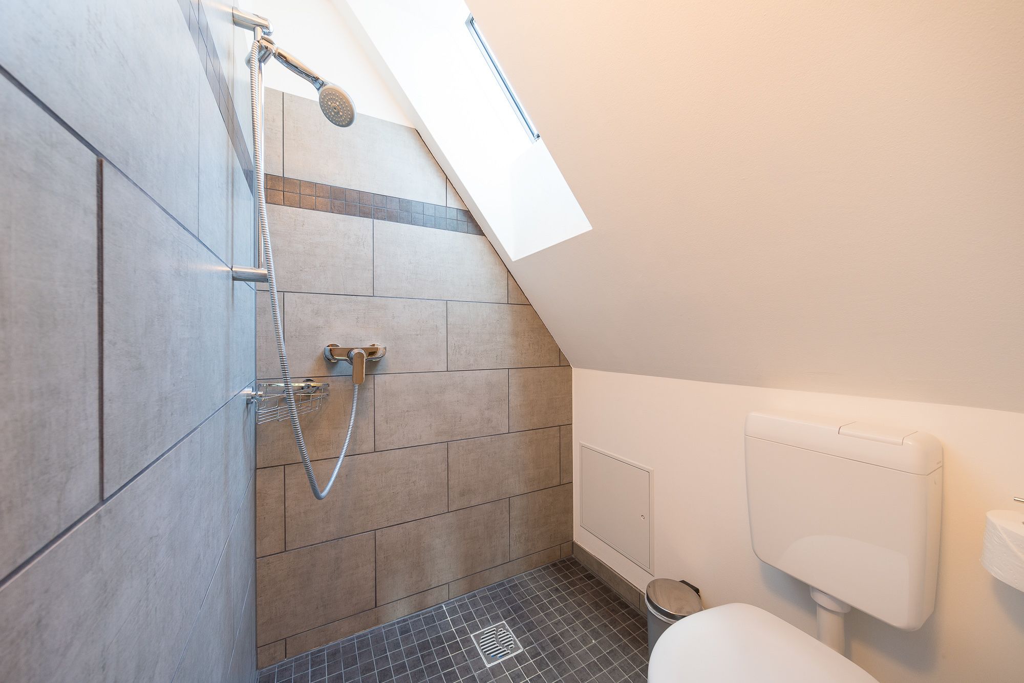 Un baño moderno con ducha, paredes con azulejos, inodoro y ventana.