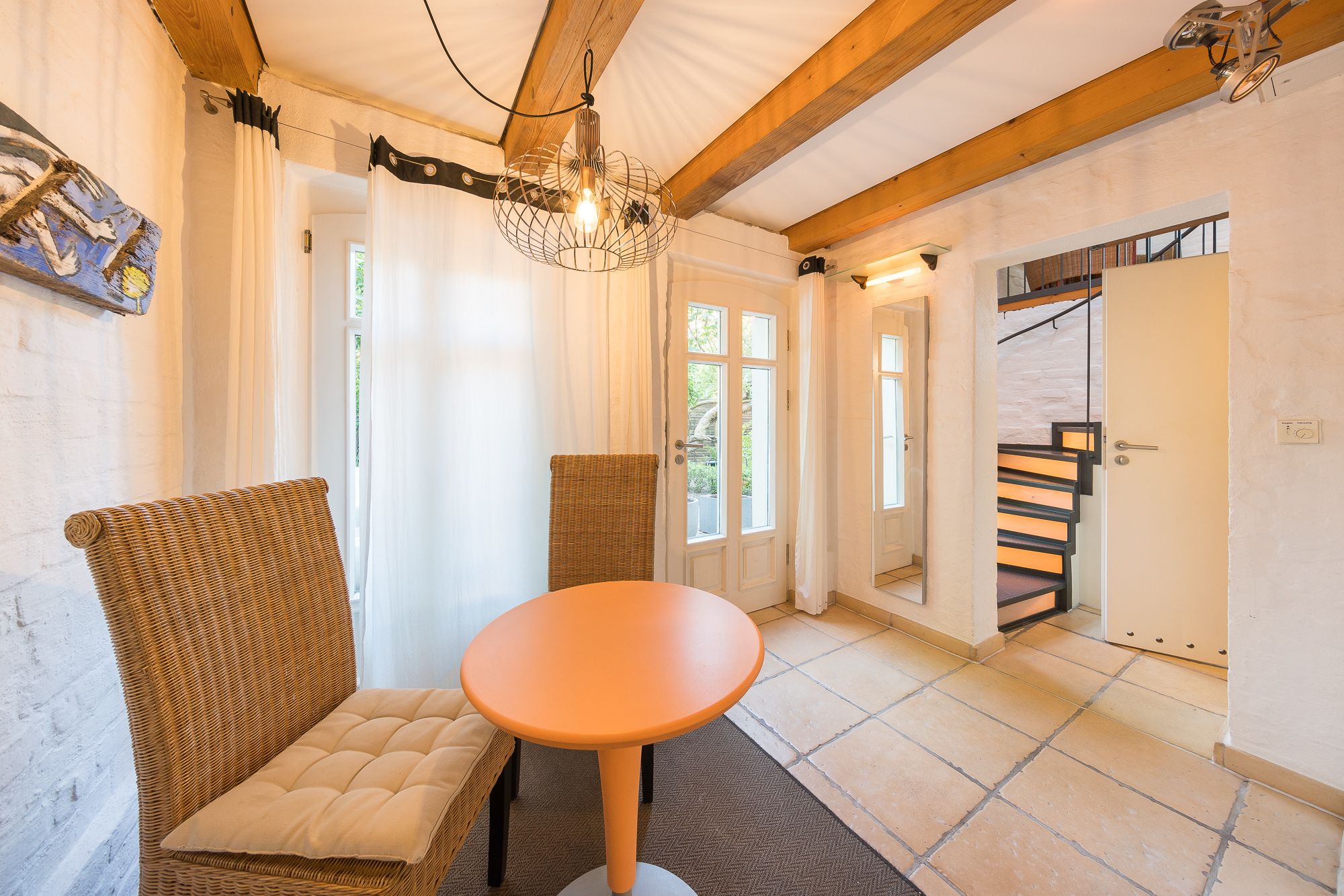 A room with wicker furniture, a round orange table, and a staircase with a wooden railing.