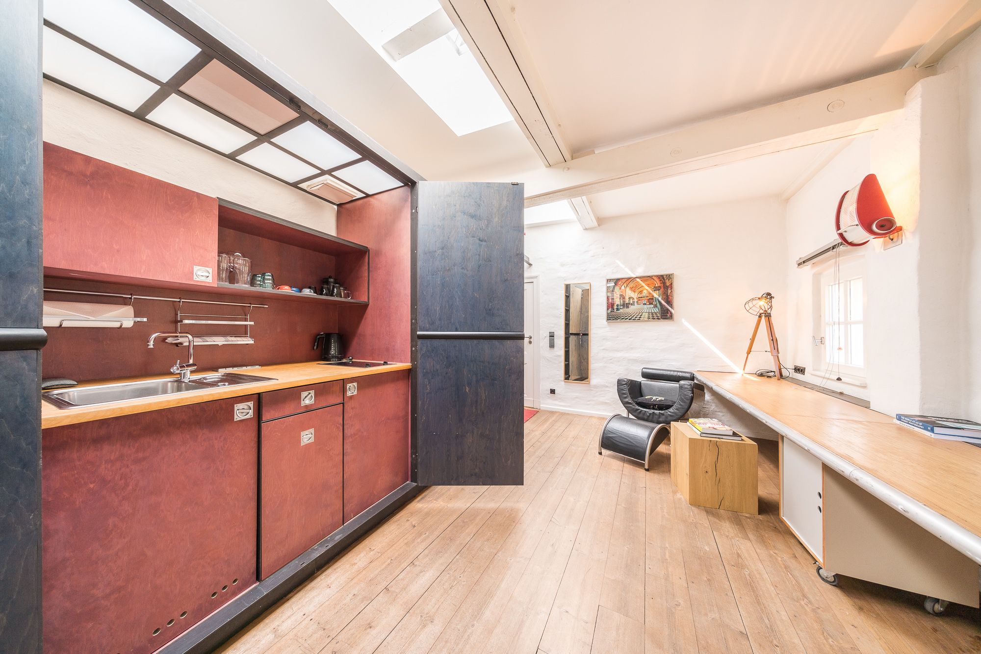 Une cuisine moderne avec un plan de travail en bois, un évier et un crédence rouge. On y trouve également un coin repas avec une chaise noire et une table.