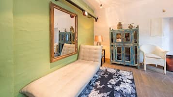 Ein Zimmer mit grüner Wand, einem großen Spiegel, einer Couch, einem Schrank mit Spiegeln, einer Lampe und einem Korbstuhl.