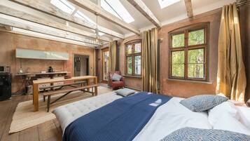 A rustic bedroom with a large bed, a wooden bench, a desk with a mirror, and a window with curtains.
